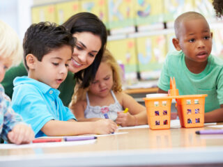 Teacher assisting diverse group of preschool children with drawing activities