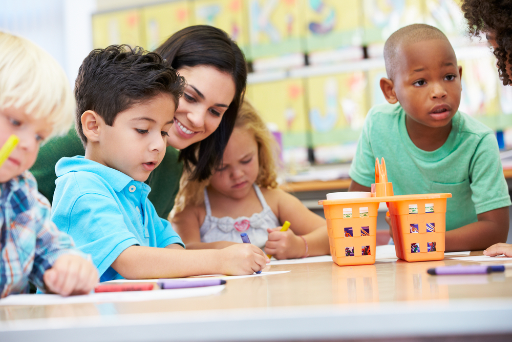 Teacher assisting diverse group of preschool children with drawing activities