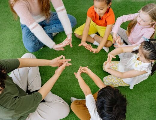 Group of children and adults sitting in a circle on the grass, doing a hand exercise