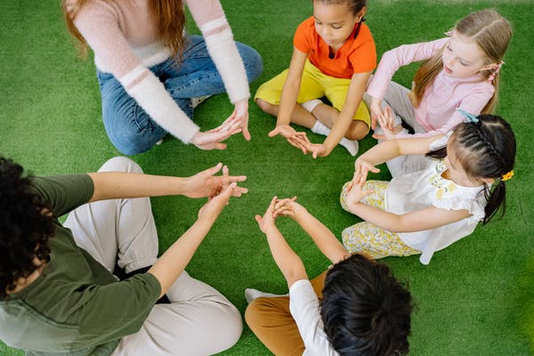 Group of children and adults sitting in a circle on the grass, doing a hand exercise