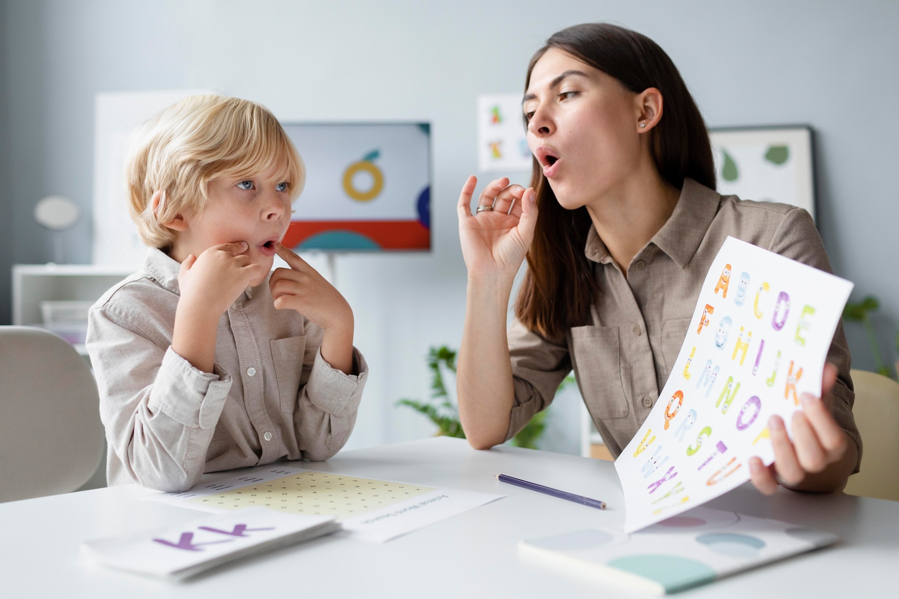 Speech therapist teaching phonetics to young boy in classroom