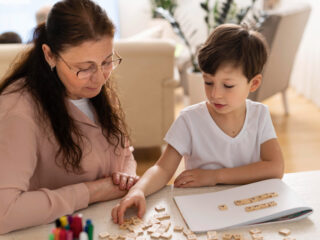 The image shows a young boy working with a teacher using letter tiles, highlighting the personalized support in special education for children with autism to develop key skills.