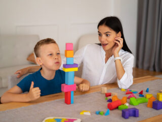 A young boy engaged in a developmental activity with colorful blocks under the guidance of an occupational therapist. The scene highlights the significance of occupational therapy for autism, demonstrating its role in enhancing fine motor skills and cognitive development.