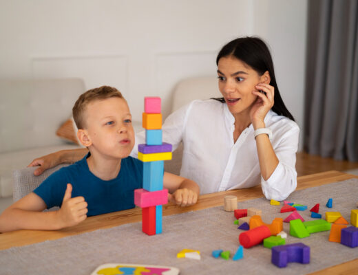 A young boy engaged in a developmental activity with colorful blocks under the guidance of an occupational therapist. The scene highlights the significance of occupational therapy for autism, demonstrating its role in enhancing fine motor skills and cognitive development.