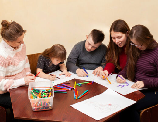 A group of children with special needs is seated around a table, drawing with colorful markers under the guidance of two adults. The scene depicts a supportive and inclusive learning environment, emphasizing the benefits of an Individualized Education Plan (IEP).