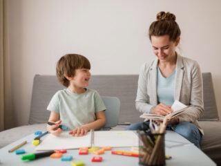 A smiling child engages with a supportive adult in a learning environment, reflecting positive autism therapy and educational support.