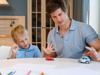 The image shows a father engaging with his young autistic son through play with toy cars, highlighting the importance of parental support and interaction in managing autism-related challenges.