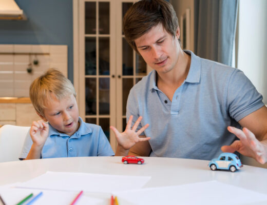 The image shows a father engaging with his young autistic son through play with toy cars, highlighting the importance of parental support and interaction in managing autism-related challenges.