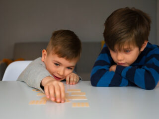 Two young boys, one with autism, playing a matching card game at a table, with one focused and the other excited.