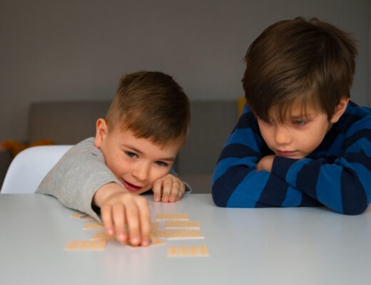 Two young boys, one with autism, playing a matching card game at a table, with one focused and the other excited.