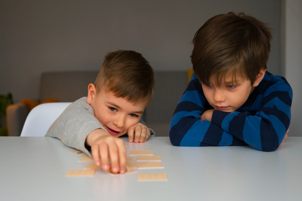 Two young boys, one with autism, playing a matching card game at a table, with one focused and the other excited.