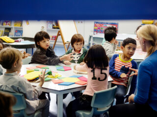 Children at a special school engaged in a hands-on activity with colorful shapes, guided by a supportive teacher in an inclusive classroom.