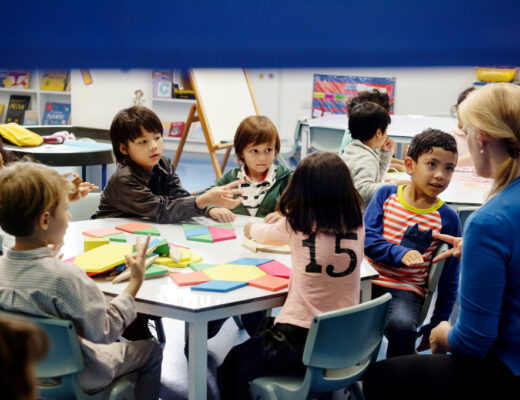 Children at a special school engaged in a hands-on activity with colorful shapes, guided by a supportive teacher in an inclusive classroom.