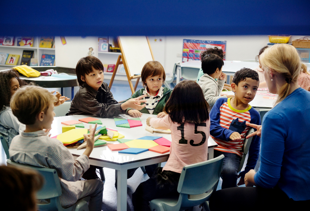 Children at a special school engaged in a hands-on activity with colorful shapes, guided by a supportive teacher in an inclusive classroom.